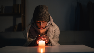 暗い部屋でニット帽を被り、キャンドルの小さな炎で凍える手を温める人物