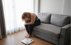 リビングで体重計を前にして、ソファに座り頭を抱えて落ち込む女性の姿