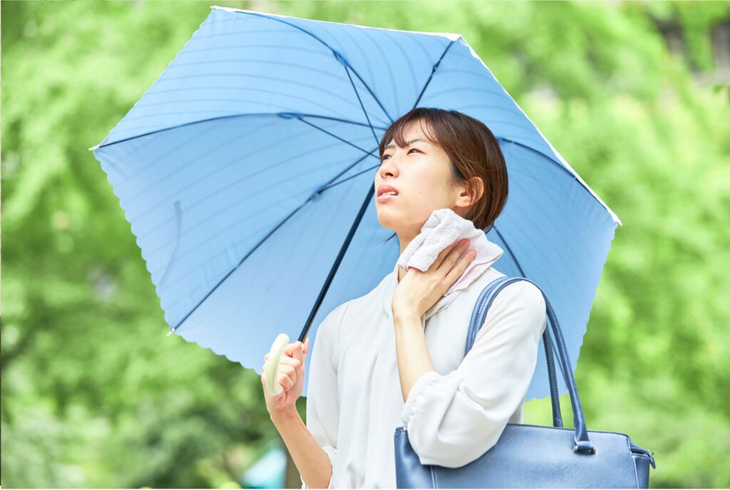 日傘をさし汗を拭う女性、夏の暑さ、熱中症、体のだるさ、夏のむくみ原因、冷え、湿度、更年期、牛久市エステ、TMR